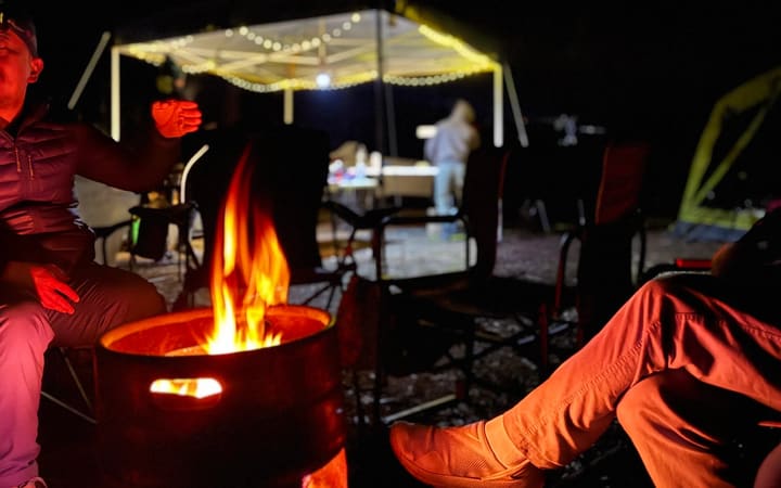 A group sitting around a campfire at night, faces lit by the flames